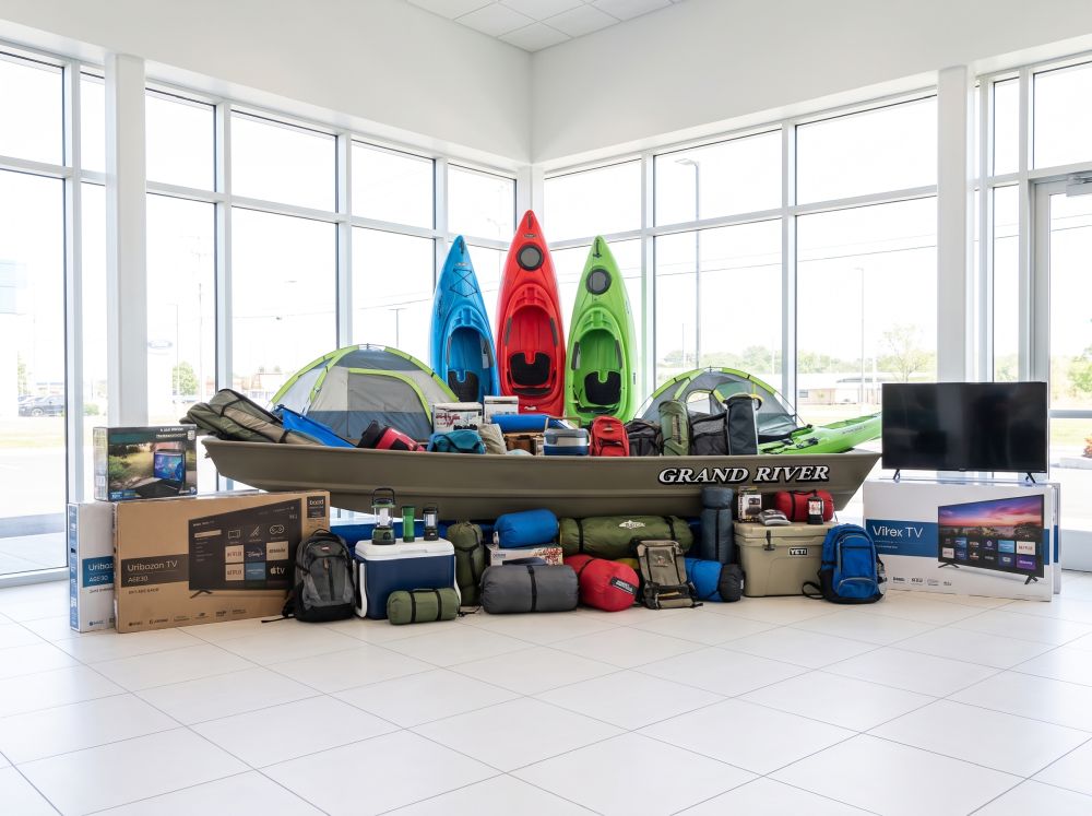 Prize Mountain stacked with kayaks, coolers and camping gear beside a boat and Chrysler, Jeep and Ram vehicles